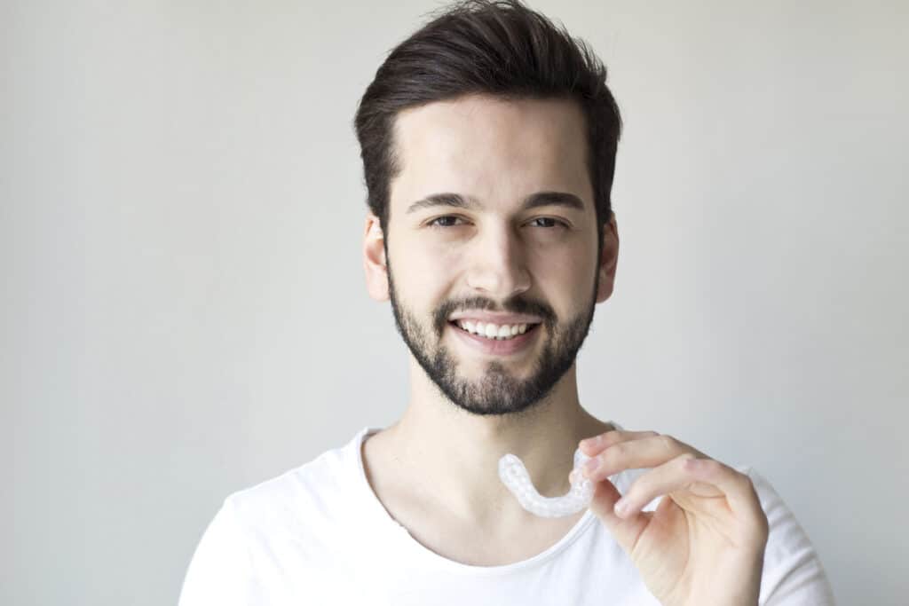 Close-up Of A Man's Hand Putting Transparent Aligner In Teeth