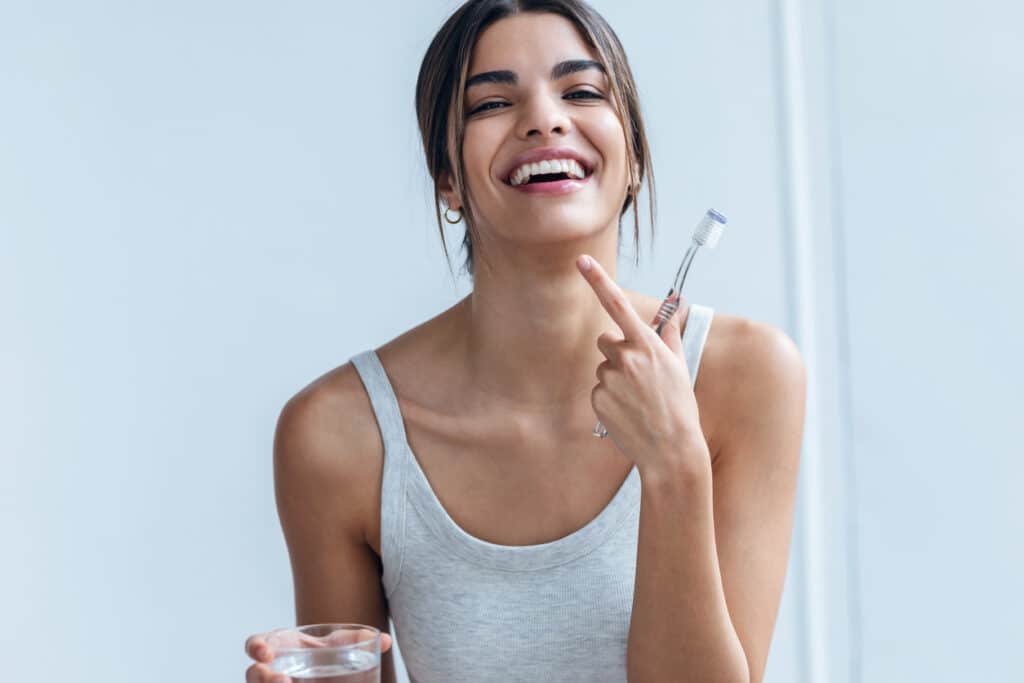 Shot of pretty young woman brushing her teeth while looking at camera in the bathroom at home.